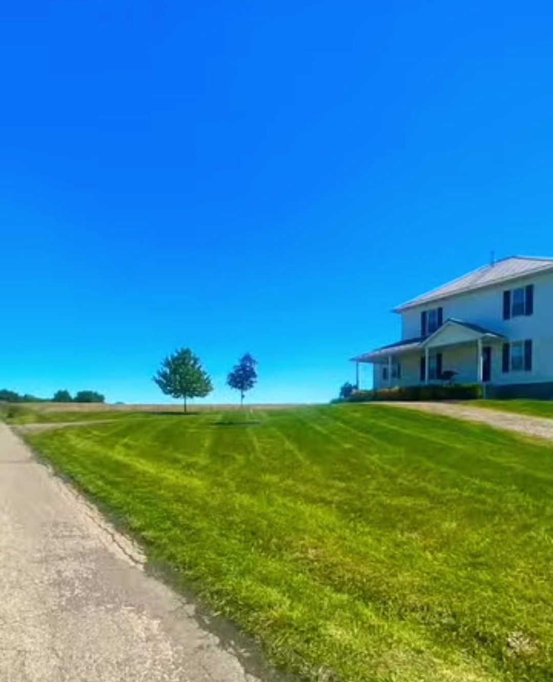 A freshly cut lawn beside a farmhouse driveway
