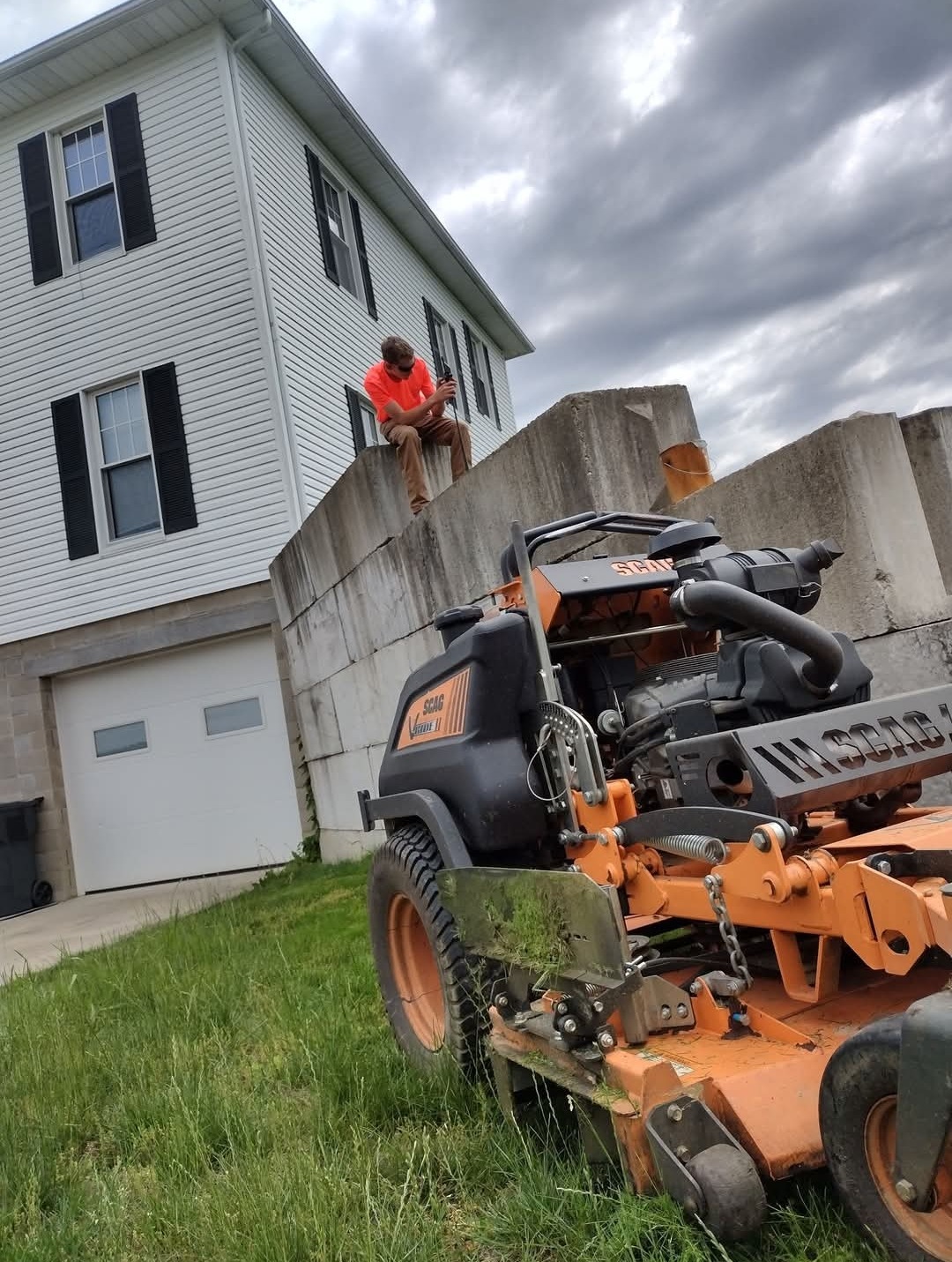 A Turf Pro crew member sitting on a wall beside their SCAG mower